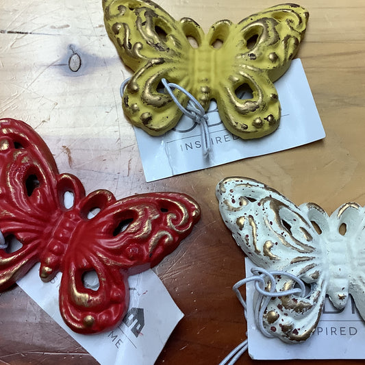 A set of three cast iron butterfly figures in red, gold, and white colors, displayed on a table with a wood surface in the background.